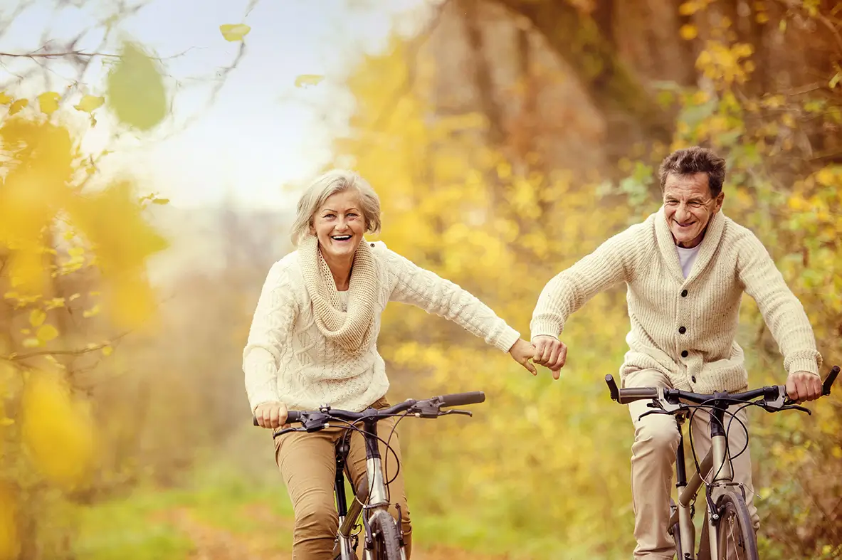 Senior couple riding bikes outdoors, smiling and enjoying retirement.